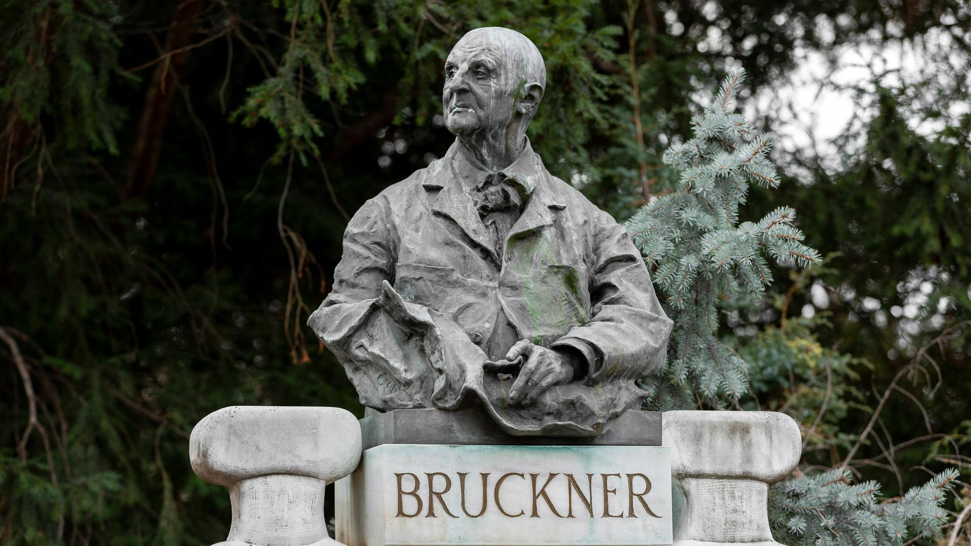 Blick auf eine Büste Bruckners, die in einem Park auf einem Sockel mit dem Schriftzug "Bruckner" ruht.