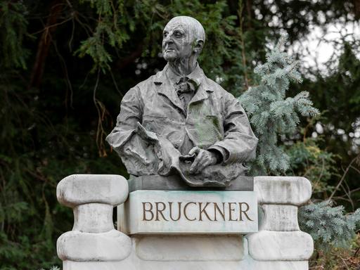 Blick auf eine Büste Bruckners, die in einem Park auf einem Sockel mit dem Schriftzug "Bruckner" ruht.