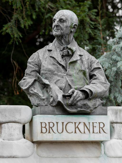 Blick auf eine Büste Bruckners, die in einem Park auf einem Sockel mit dem Schriftzug "Bruckner" ruht.