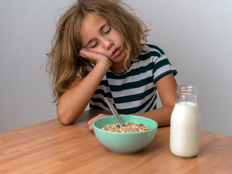 Ein Mädchen sitzt an einem Tisch und schläft über dem Frühstück ein