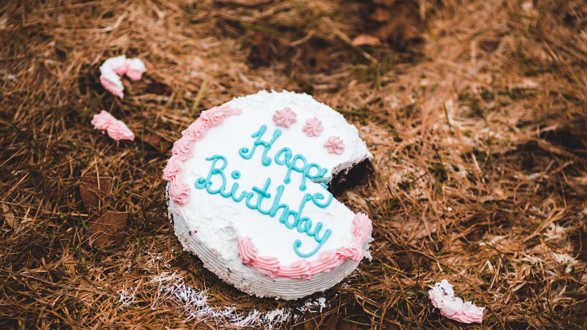 Eine Torte mit der Aufschrift Happy Birthday liegt auf dem Boden. Ein Stück fehlt und liegt in kleinen Teilen verstreut daneben.