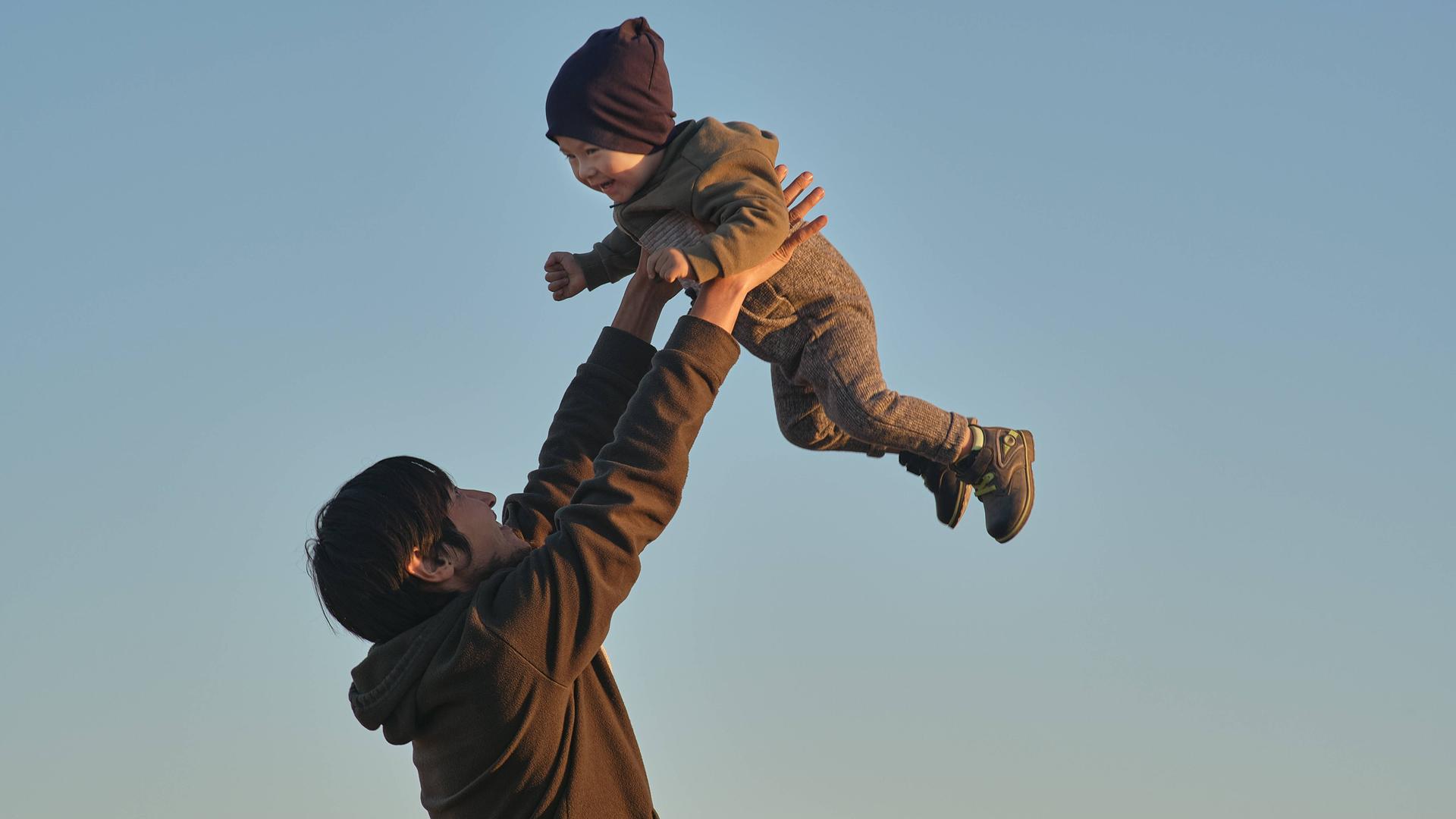 Ein glücklicher Mann hebt seinen lachenden kleinen Sohn in die Höhe.