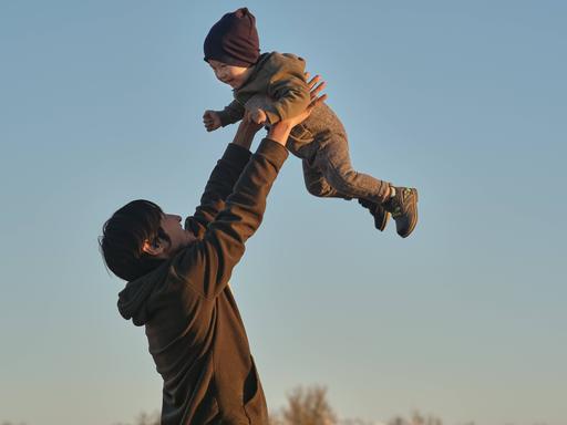 Ein glücklicher Mann hebt seinen lachenden kleinen Sohn in die Höhe.