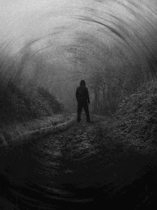 Dunkles Schwarz-Weiß-Bild mit der Silhouette eines Manns, der in der Landschaft steht, von hinten