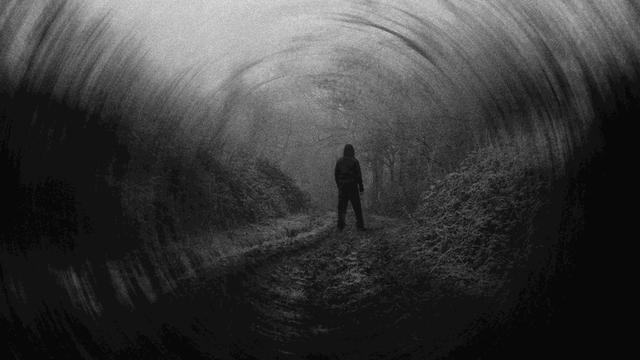 Dunkles Schwarz-Weiß-Bild mit der Silhouette eines Manns, der in der Landschaft steht, von hinten