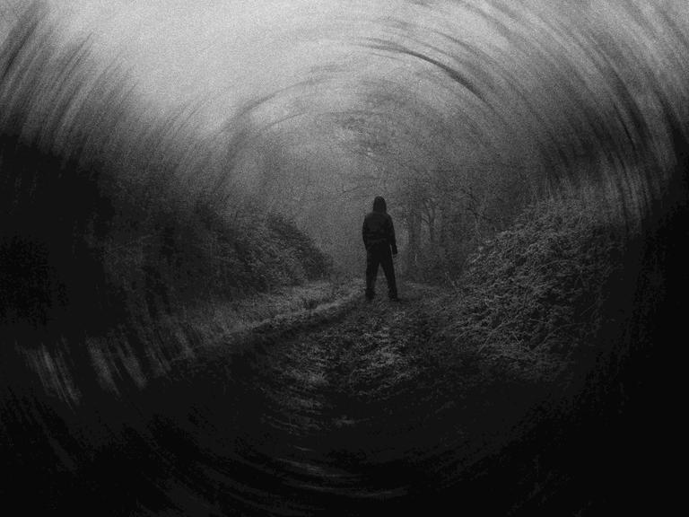 Dunkles Schwarz-Weiß-Bild mit der Silhouette eines Manns, der in der Landschaft steht, von hinten