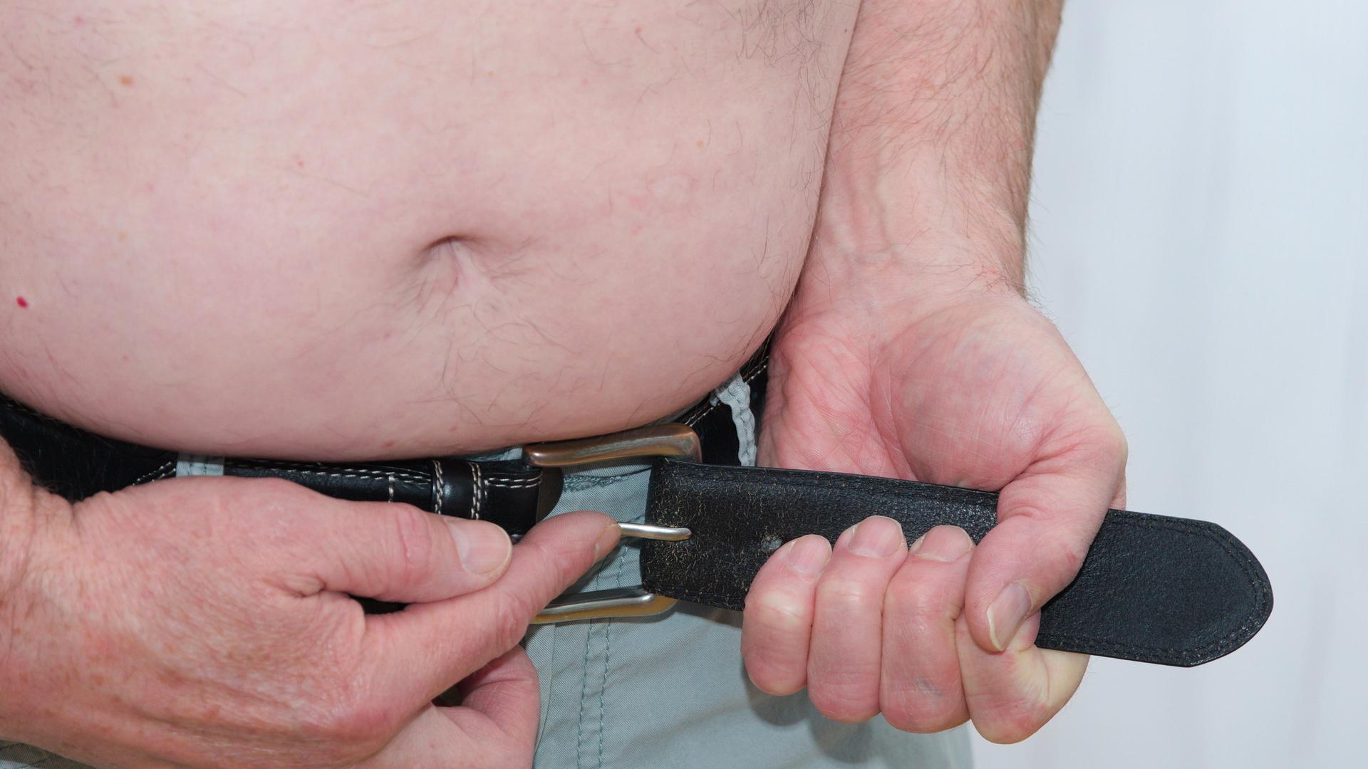 Ein Mann schnallt seinen Gürtel enger. Darüber sieht man einen nackten Bauch. Der Bauch hängt leicht über den Gürtel. Ein Mann schnallt seinen Gürtel enger. Darüber sieht man einen nackten Bauch. Der Bauch hängt leicht über den Gürtel.
