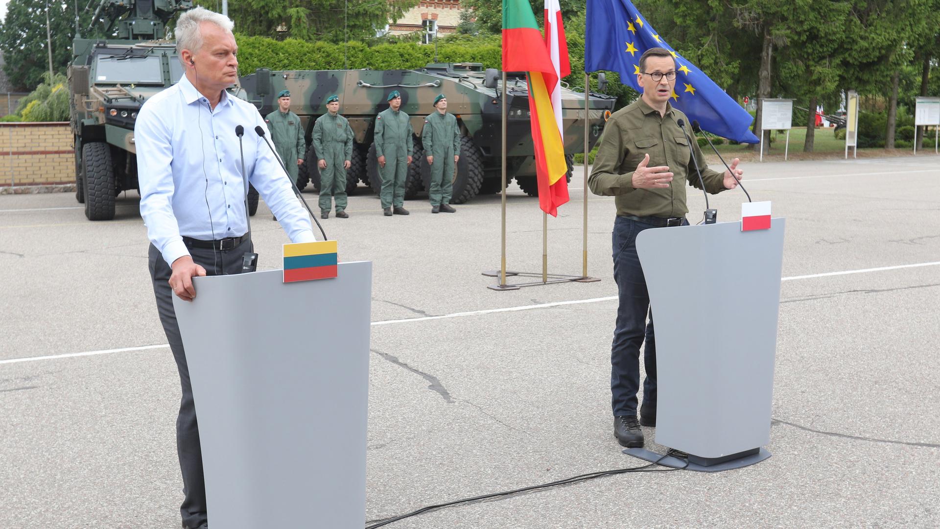 Litauens Präsident Nauseda und der polnische Premier Morawiecki stehen an Rednerpulten. Im Hintergrund sind Militärfahrzeuge und militärisches Personal zu sehen.