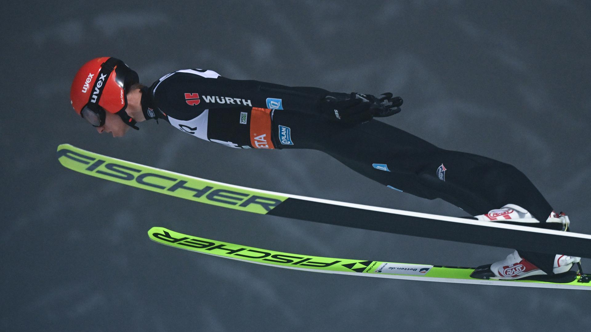 Karl Geiger im Sprung. Er ist tief über seine Ski gebeugt.