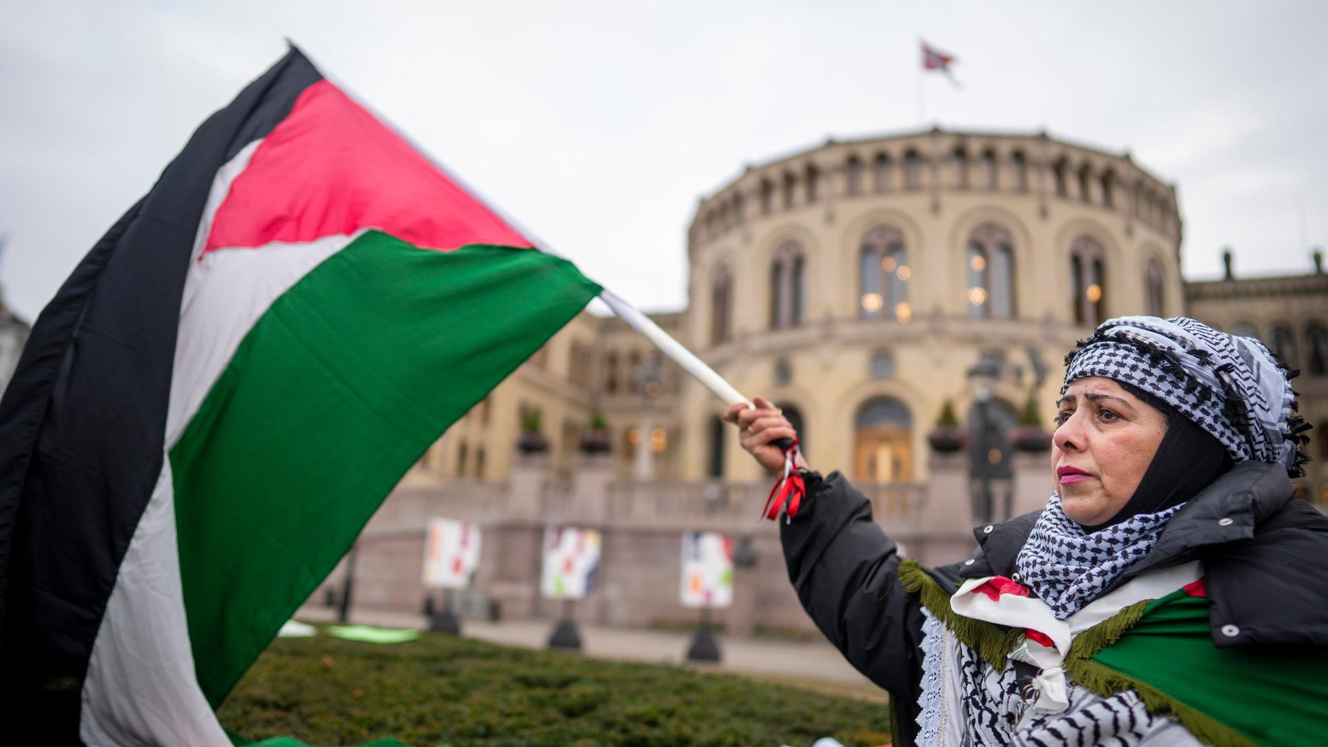 Eine Frau steht mit einer palästinensischen Flagge vor dem Parlamentsgebäude in Norwegen.