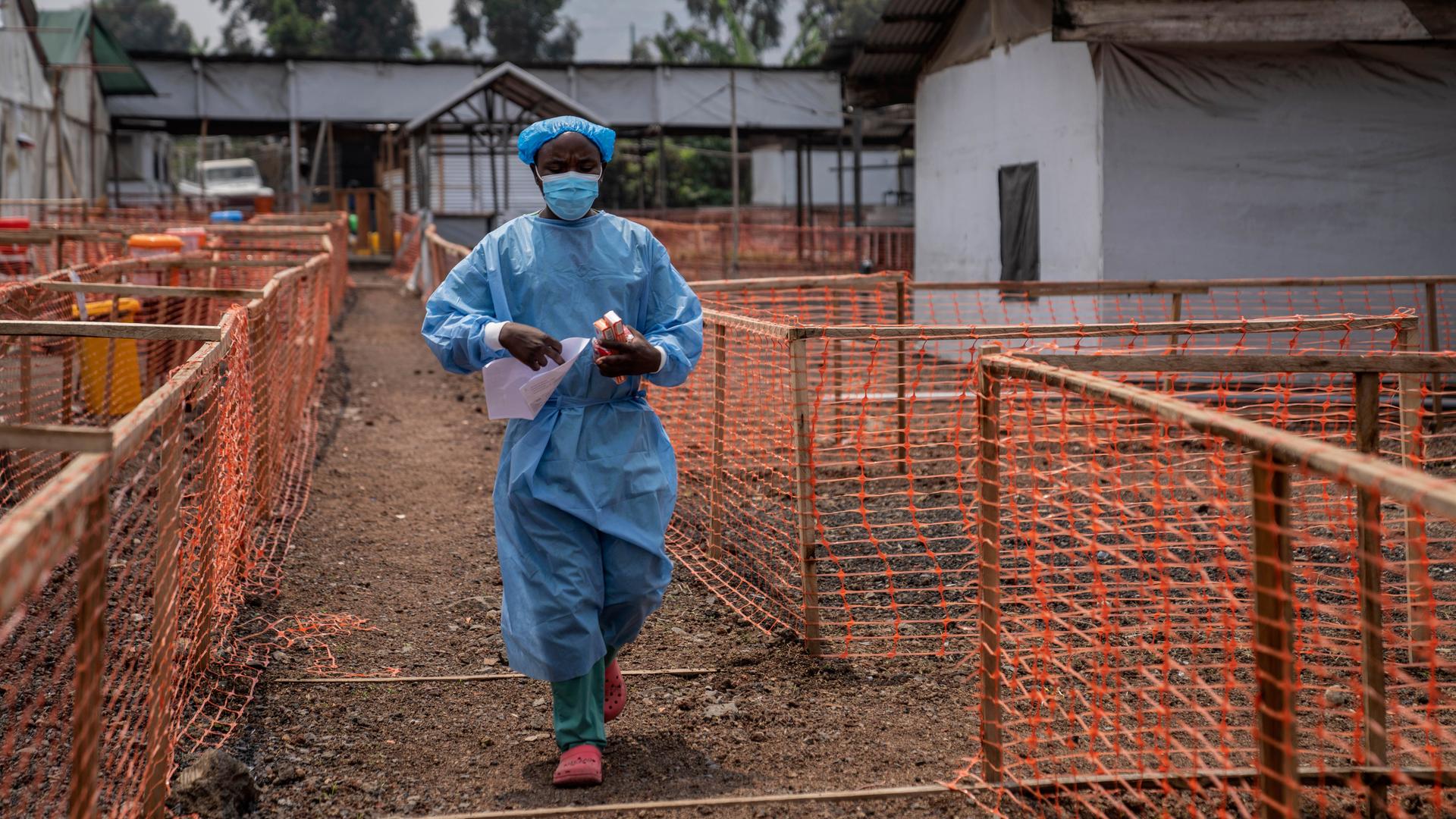 Ein Mitarbeiter in einem Gesundheitszentrum im Kongo. Er trägt einen Mundschutz und einen blauen Plastikkittel. In den Händen hält er Medikamente.