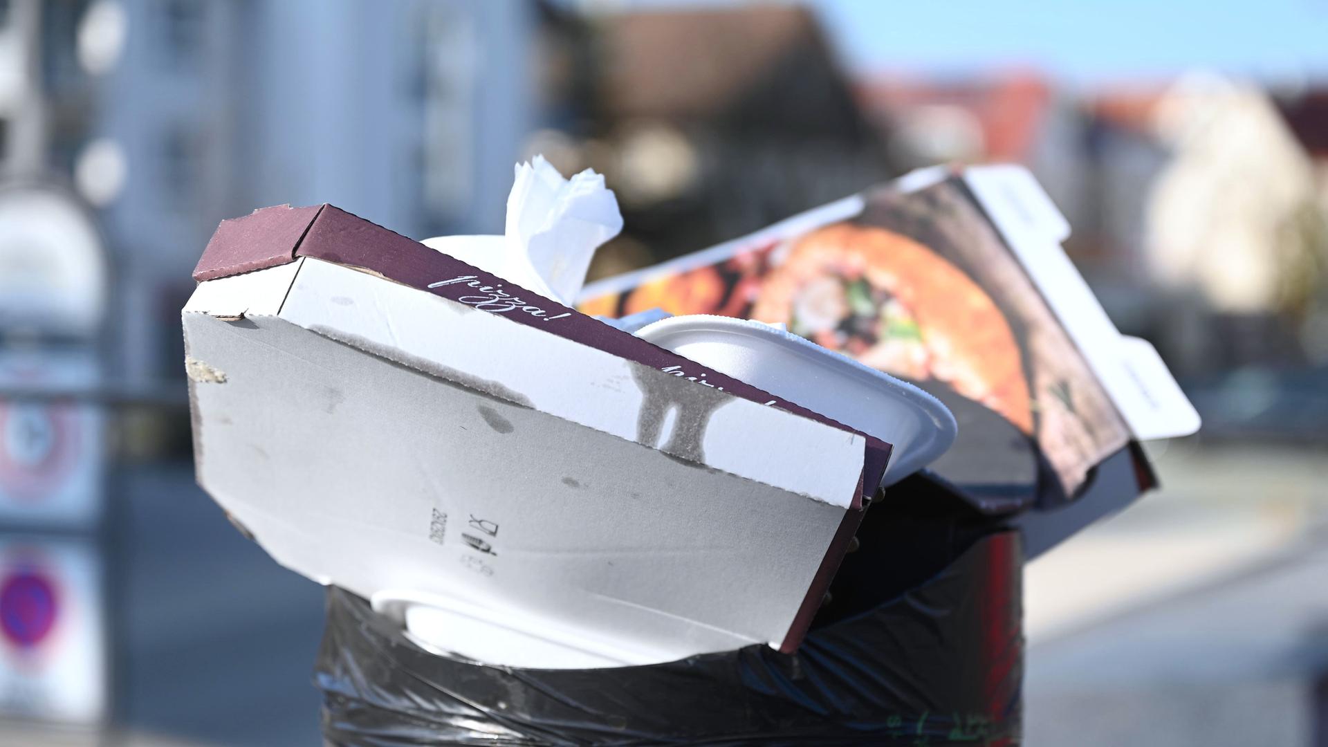 Pizzakartons und andere Essensverpackungen stecken in einem öffentlichen Mülleimer