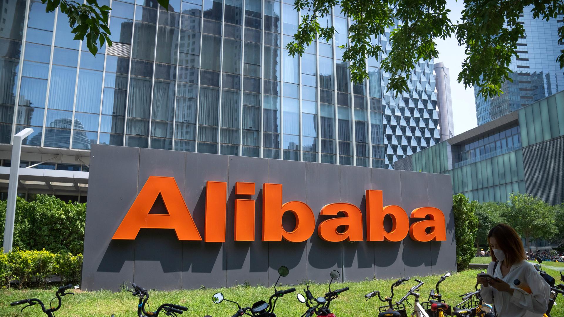 Der Schriftzug "Alibaba" steht vor einem gläseren Gebäude. Im Vordergrund stehen einige Fahrräder. Der Schriftzug "Alibaba" steht vor einem gläseren Gebäude. Im Vordergrund stehen einige Fahrräder.