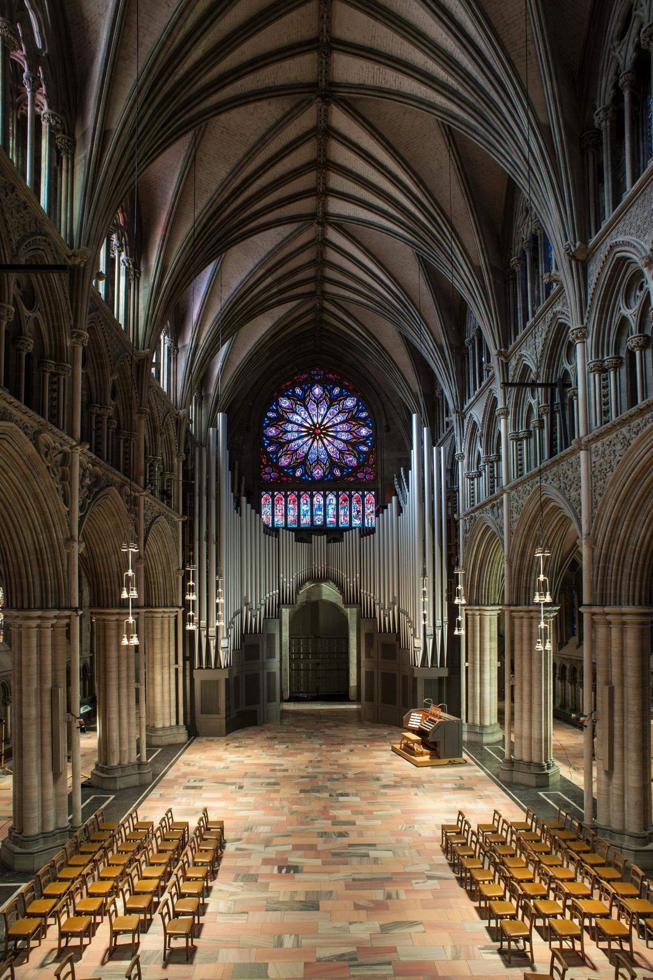 Im Innern eines gotischen Kirchenschiffs sind Stuhlreihen sowie am hinteren Ende ein Orgelspieltisch unterhalb einer großen Orgel zu sehen. Darüber fällt der Blick auf ein riesiges, buntes Rosettenfenster.