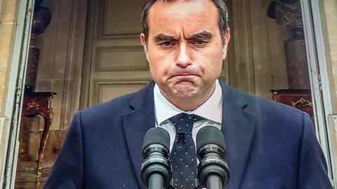 Ein Foto von einem Fernseh-Bildschirm. Auf dem Bildschirm ist der französische Regierungs-Chef Lecornu zu sehen. Er steht vor Mikrofonen und presst die Lippen aufeinander. Er sieht sehr unzufrieden aus. 