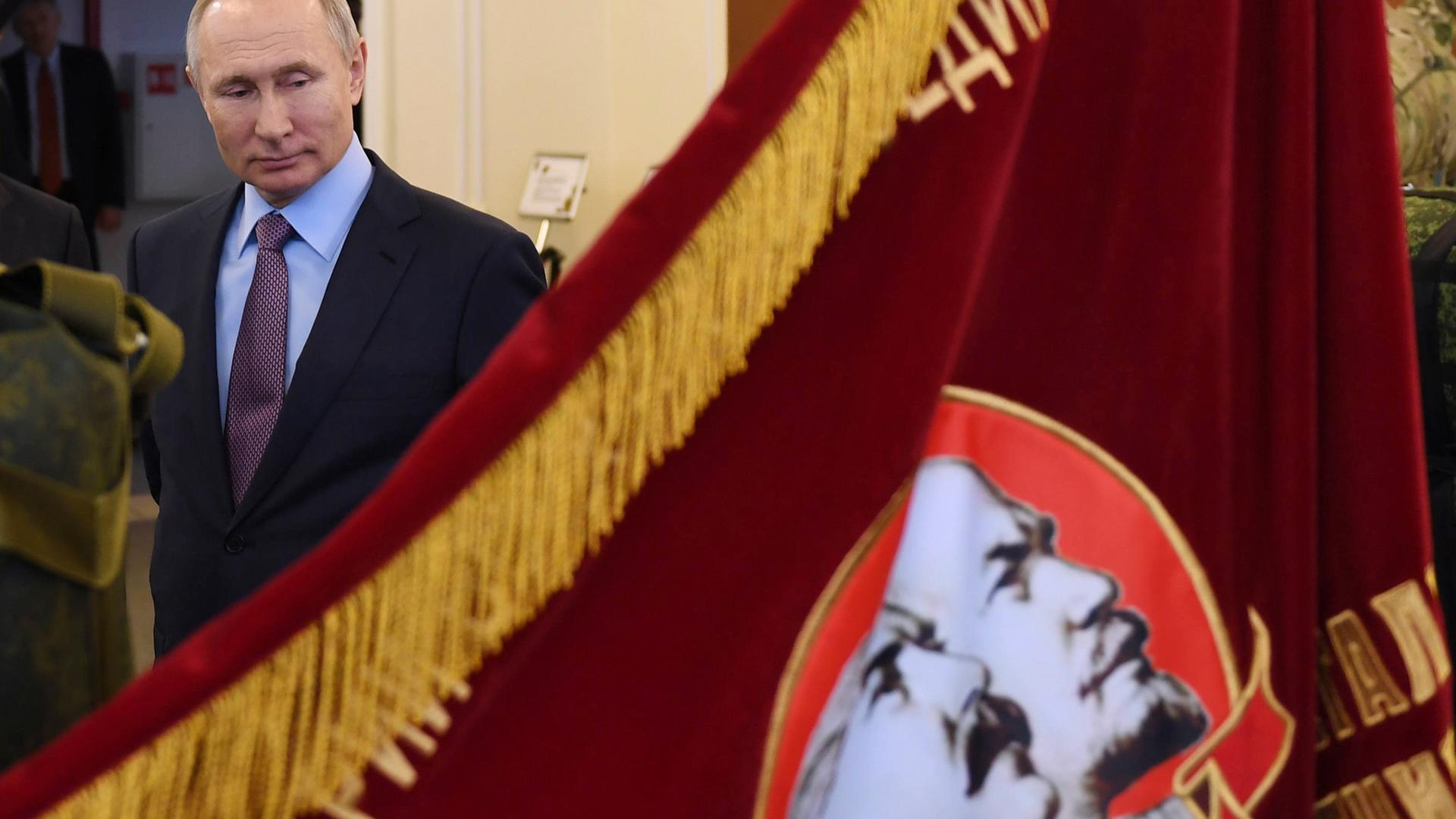 Der russische Präsident Wladimir Putin schaut auf ein Banner aus der Zeit der Sowjetunion, auf der Lenin und Stalin zu sehen sind.