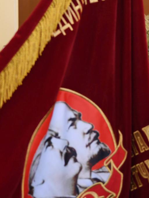Der russische Präsident Wladimir Putin schaut auf ein Banner aus der Zeit der Sowjetunion, auf der Lenin und Stalin zu sehen sind.