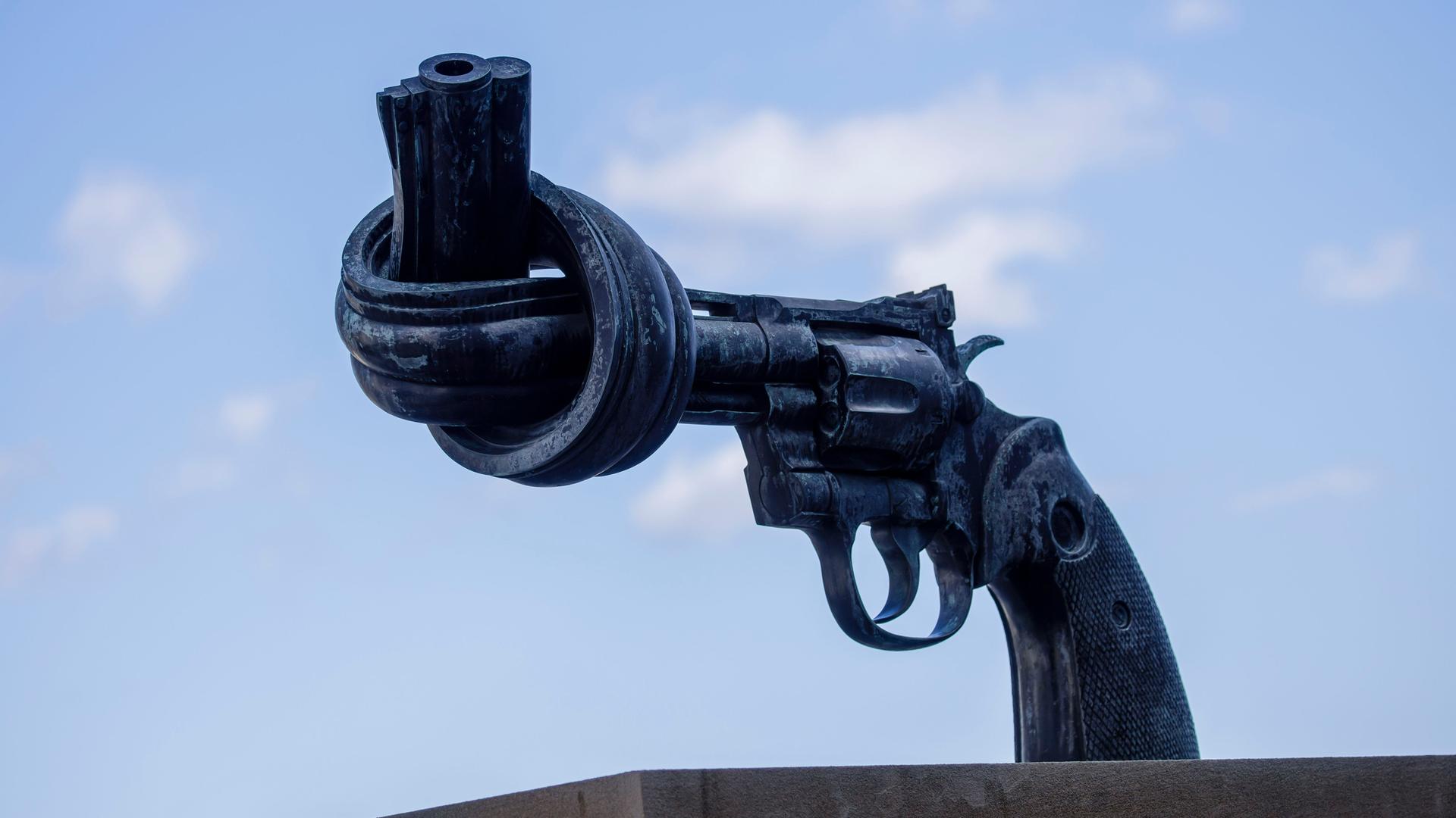 Eine Skulptur symbolisiert einen Revolver. Dessen Lauf sist zu einem Knoten verbogen. Die Skulptur steht vor dem Hauptgebäude der Vereinten Nationen in New York.