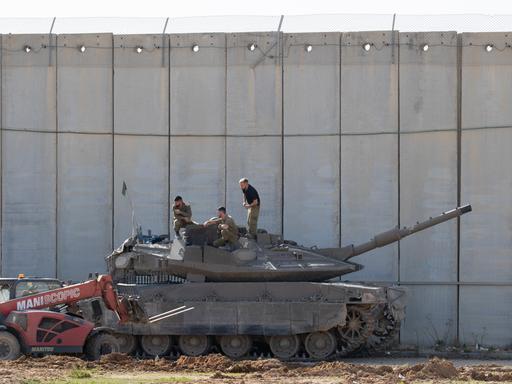 Israelische Soldaten führen am 23. November 2023 im Schatten der Zementmauer, die Israel vom Gazastreifen trennt, Wartungsarbeiten an einem Merkava-Panzer durch. 