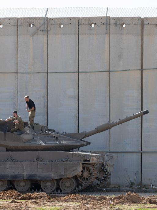 Israelische Soldaten führen am 23. November 2023 im Schatten der Zementmauer, die Israel vom Gazastreifen trennt, Wartungsarbeiten an einem Merkava-Panzer durch. 