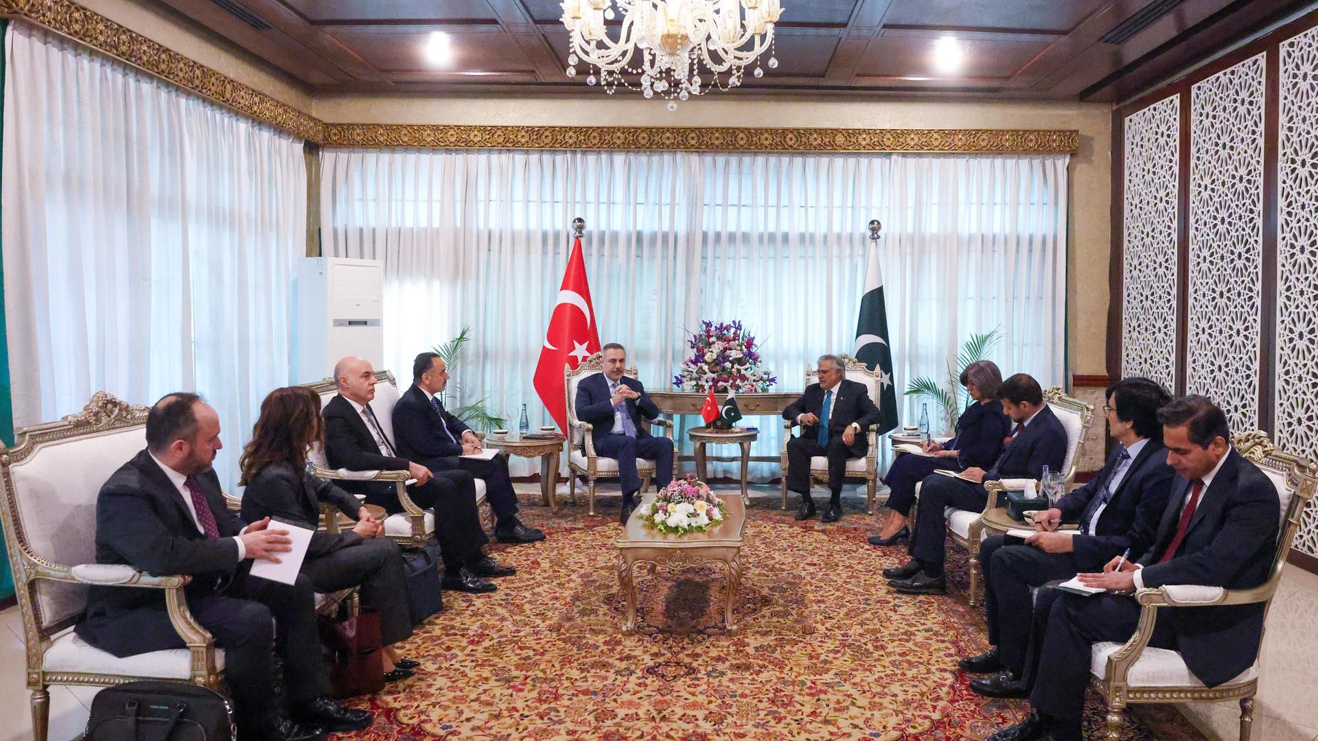 Der türkische Außenminister Hakan Fidan (5. von links) trifft sich in Islamabad mit dem pakistanischen Außenminister Muhammad Ishaq Dar (5. von rechts). Sie sitzen zusammen mit weiteren Staatsbeamten im Kreis um einen Tisch. 