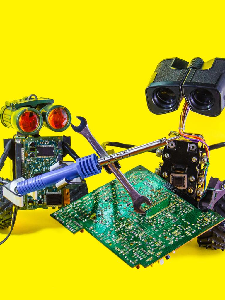 Zwei fröhliche spielzeugartige Roboter reparieren eine Leiterplatte mit Lötkolben vor knallgelbem Hintergrund. 
