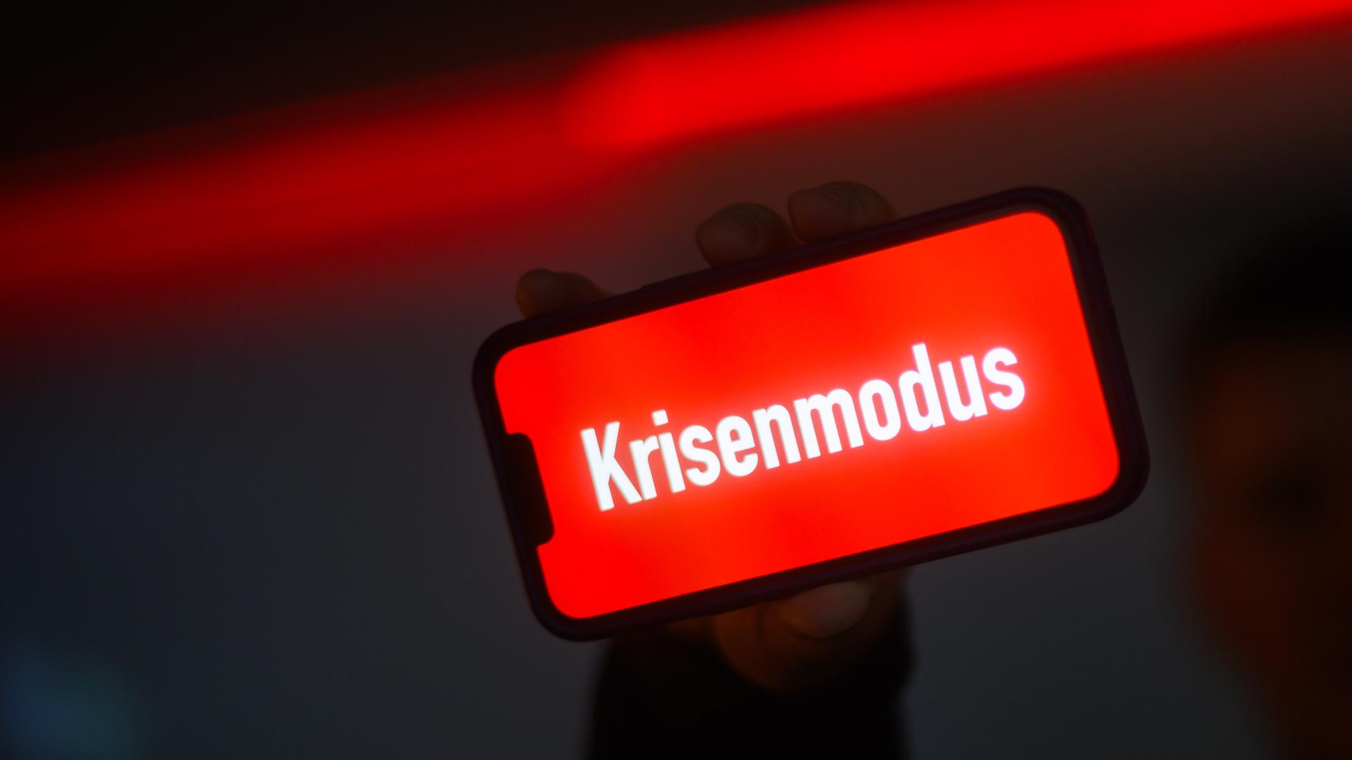 Das Wort "Krisenmodus" steht auf einem Bildschirm von einem Handy. Das Wort ist weiß, der Hintergrund rot.
