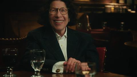 Die New Yorker Essayistin Fran Lebowitz sitzt an einem Tisch in einem Restaurant und lächelt.
