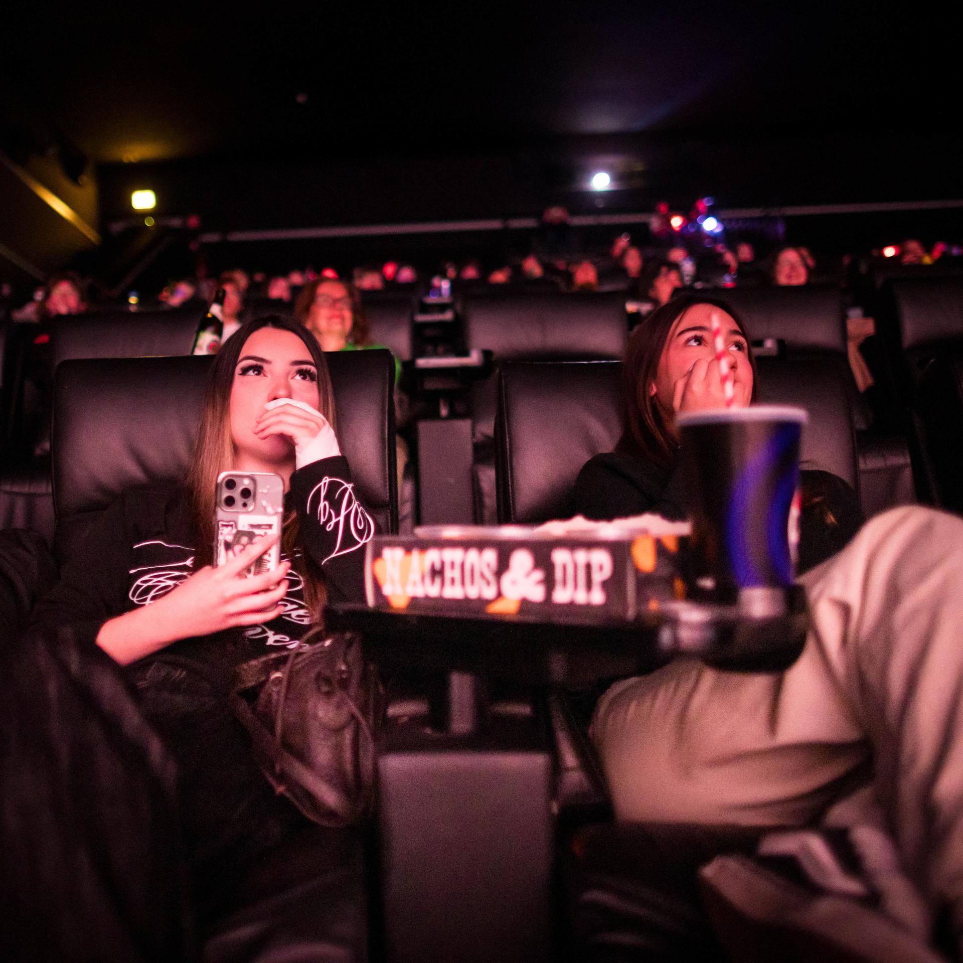 Blick auf die Zuschauerreihen mit der ersten Reihe im Vordergrund: Drei junge Frauen schauen nach vorne und essen dabei Popcorn. 