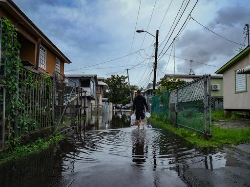 Ein Mann mit Einkaufstüten läuft durch eine überflutete Straße im Viertel Juana Matos in Catano, Puerto Rico.