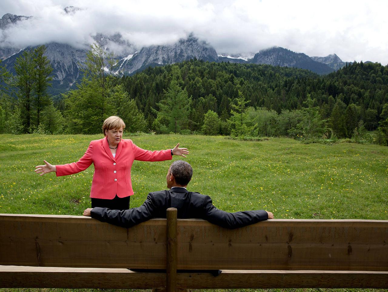 Angela Merkel breitet vor Barack Obama die Arme aus, hinter ihr Berge.