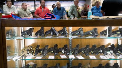 Glasvitirinen mit Revolvern und Schnellfeuerwaffen in einem Waffenladen in den USA. Im Hintergrund stehen männliche Kunden Schlange.