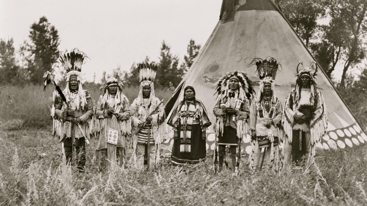 Jun. 06, 1913 - USA - Group of Siksika (Blackfeet) men and one woman singing in front of tipi - Moki rain maker and chief in costume, World's Fair, St. Louis, 1904