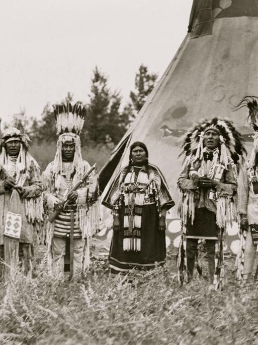 Jun. 06, 1913 - USA - Group of Siksika (Blackfeet) men and one woman singing in front of tipi - Moki rain maker and chief in costume, World's Fair, St. Louis, 1904