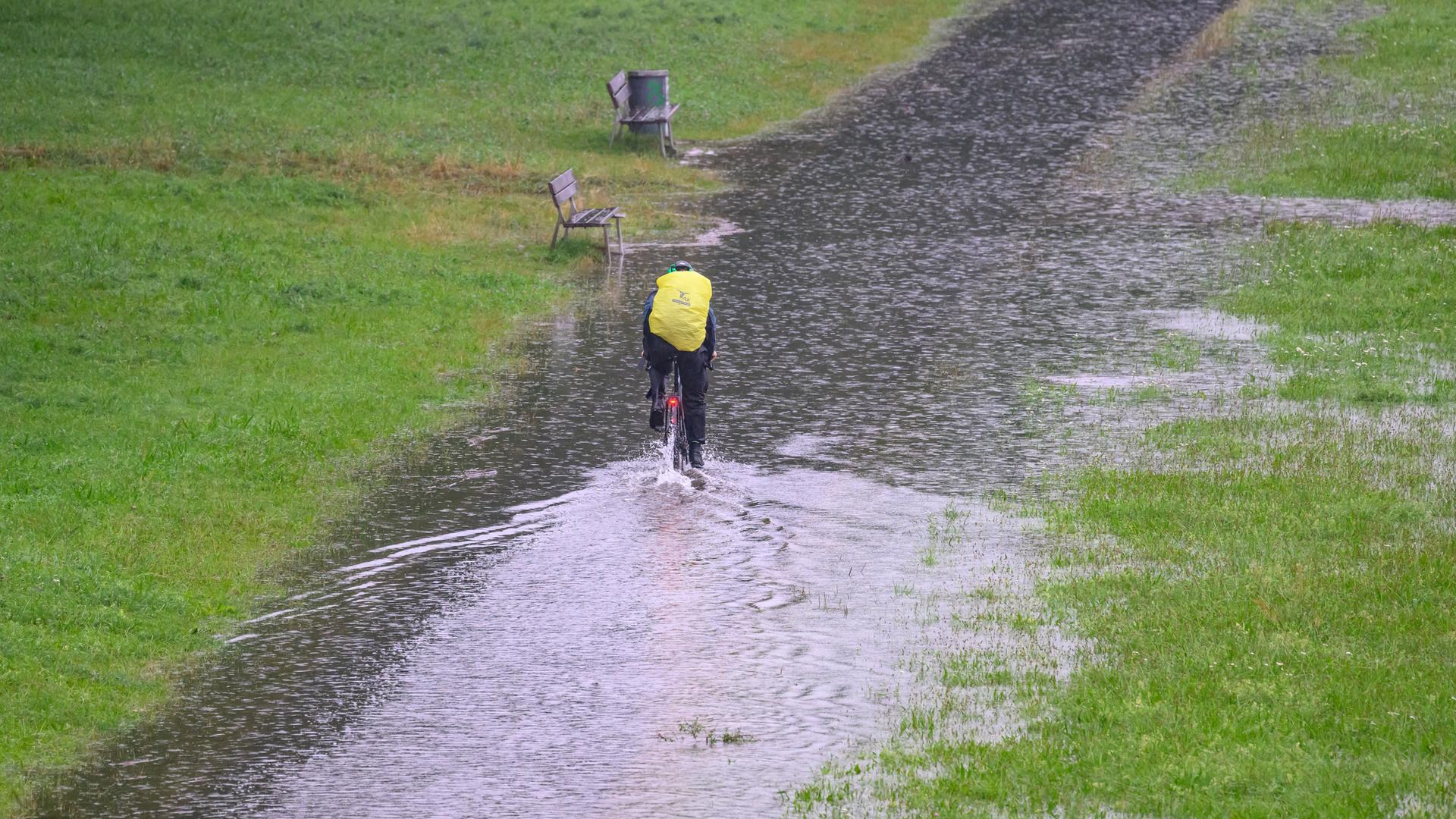 Ein Radfahrer fährt auf einem Radweg entlang, der vom Hochwasser der Elbe überflutet ist. Er trägt Regenkleidung und hat einen Überzug über seinen Rucksack gespannt.