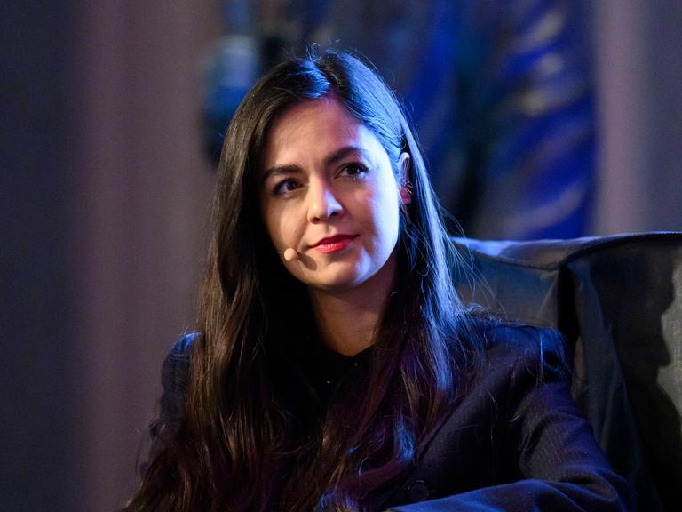 Shahrzad Osterer, mit einem Ansteckmikrofon, im dunklen Sakko, nimmt an einer Podiumsdiskussion teil.