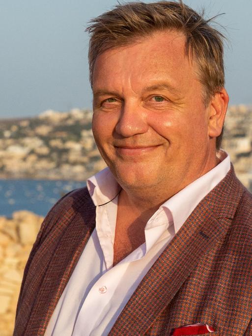 Hape Kerkeling steht lächelnd vor dem Panorama der Mittelmeerinsel Malta.
