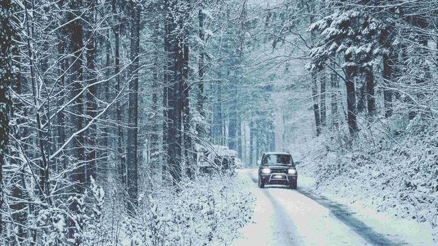 Eine verschneite Straße im Tannenwald, darauf fährt ein Auto.