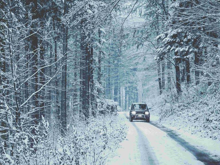 Eine verschneite Straße im Tannenwald, darauf fährt ein Auto.