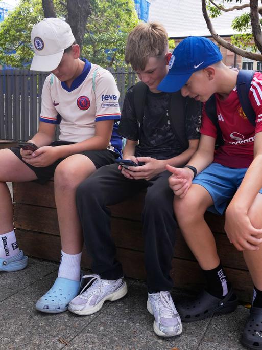 Minderjährige Kinder sitzen auf einer Bank und gucken ins Handy