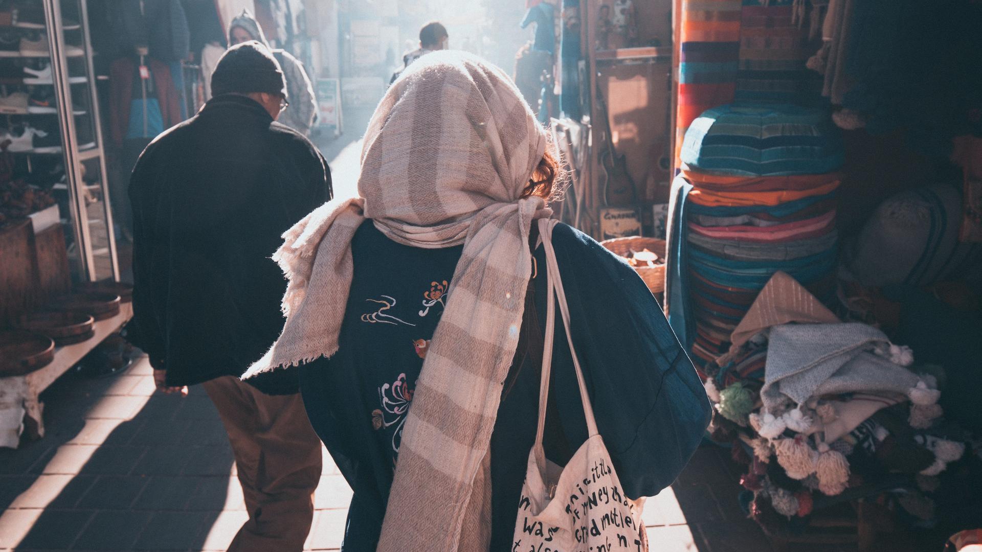 Eine Frau und ein Mann gehen in einer Stadt in Marokko eine Marktgasse entlang. 