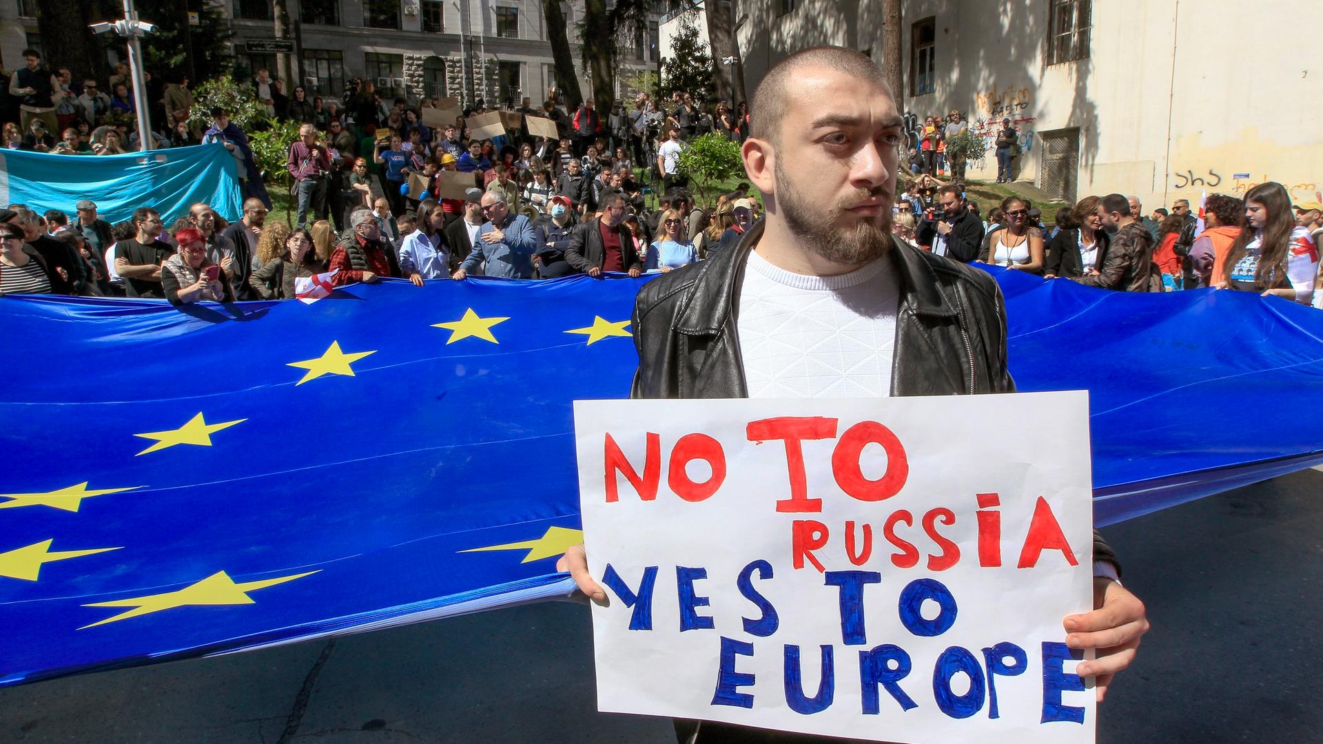 Ein Mann steht vor Demonstranten mit einer riesigen EU-Flagge. Er hält ein Pappschild mit der Aufschrift "No to Russia, yes to Europe".