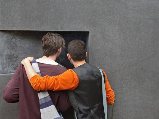 Zwei Männer stehen Arm in Arm vor dem Denkmal für die im Nationalsozialismus verfolgten Homosexuellen in Berlin.  