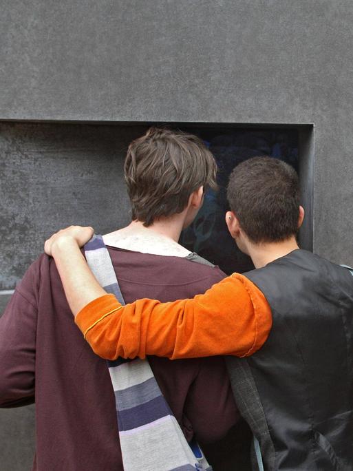 Zwei Männer stehen Arm in Arm vor dem Denkmal für die im Nationalsozialismus verfolgten Homosexuellen in Berlin.  