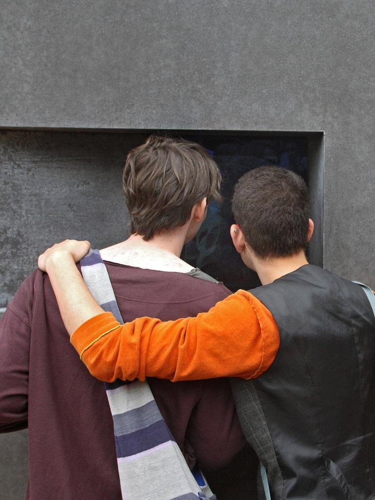 Zwei Männer stehen Arm in Arm vor dem Denkmal für die im Nationalsozialismus verfolgten Homosexuellen in Berlin.  