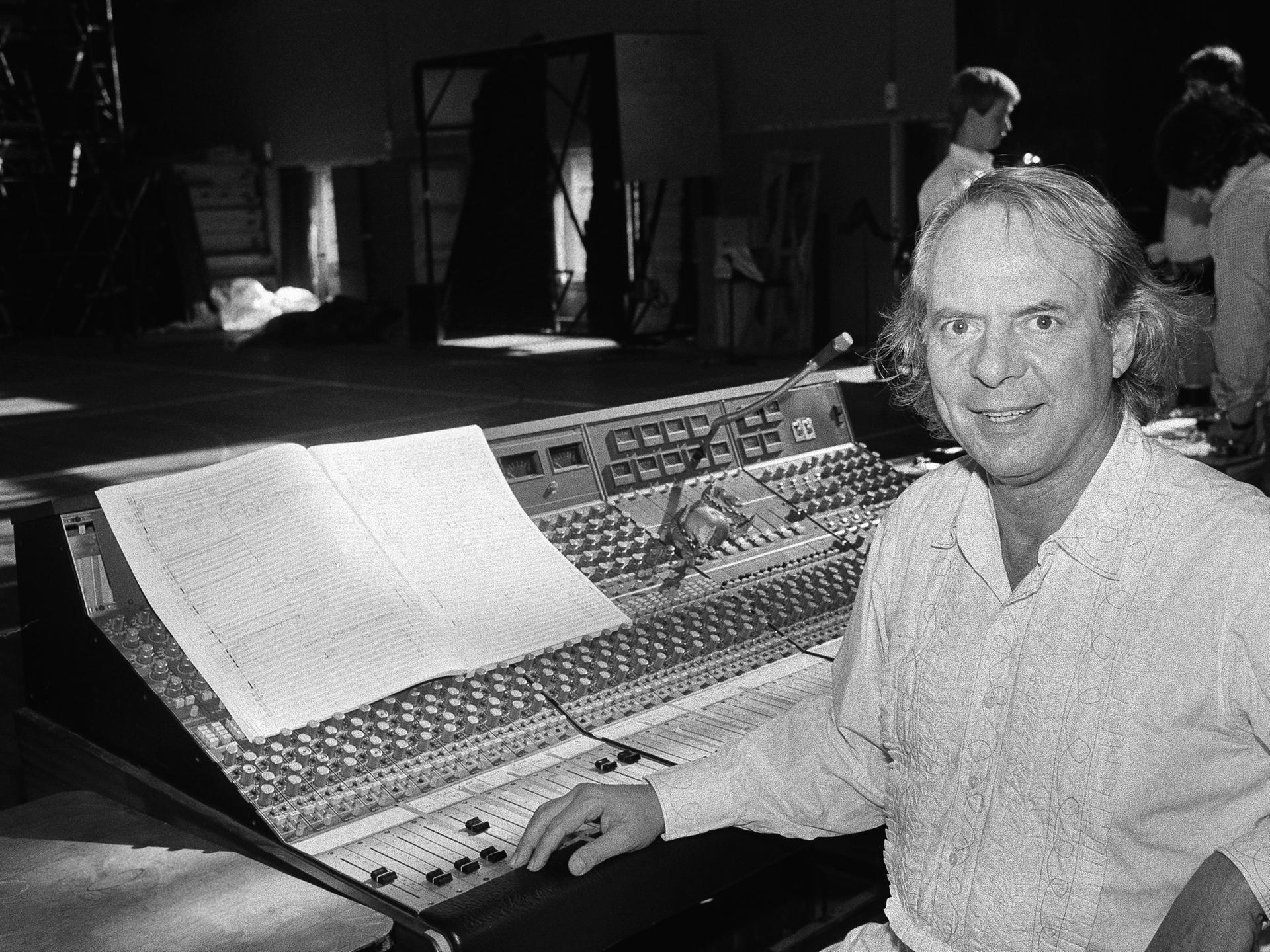 Der Komponist Karlheinz Stockhausen sitzt in die Kamera lächelnd an einem großen Pult im Royal Opera House, London.