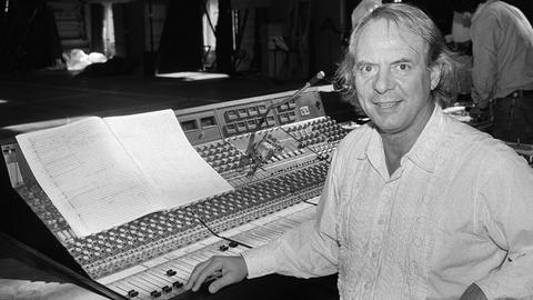 Der Komponist Karlheinz Stockhausen sitzt in die Kamera lächelnd an einem großen Pult im Royal Opera House, London.
