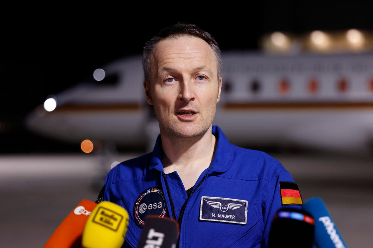 Der deutsche Astronaut Matthias Maurer steht im blauen Overall auf dem Rollfeld vor einem Flugzeug und wird interviewt Der deutsche Astronaut Matthias Maurer steht im blauen Overall auf dem Rollfeld vor einem Flugzeug und wird interviewt
