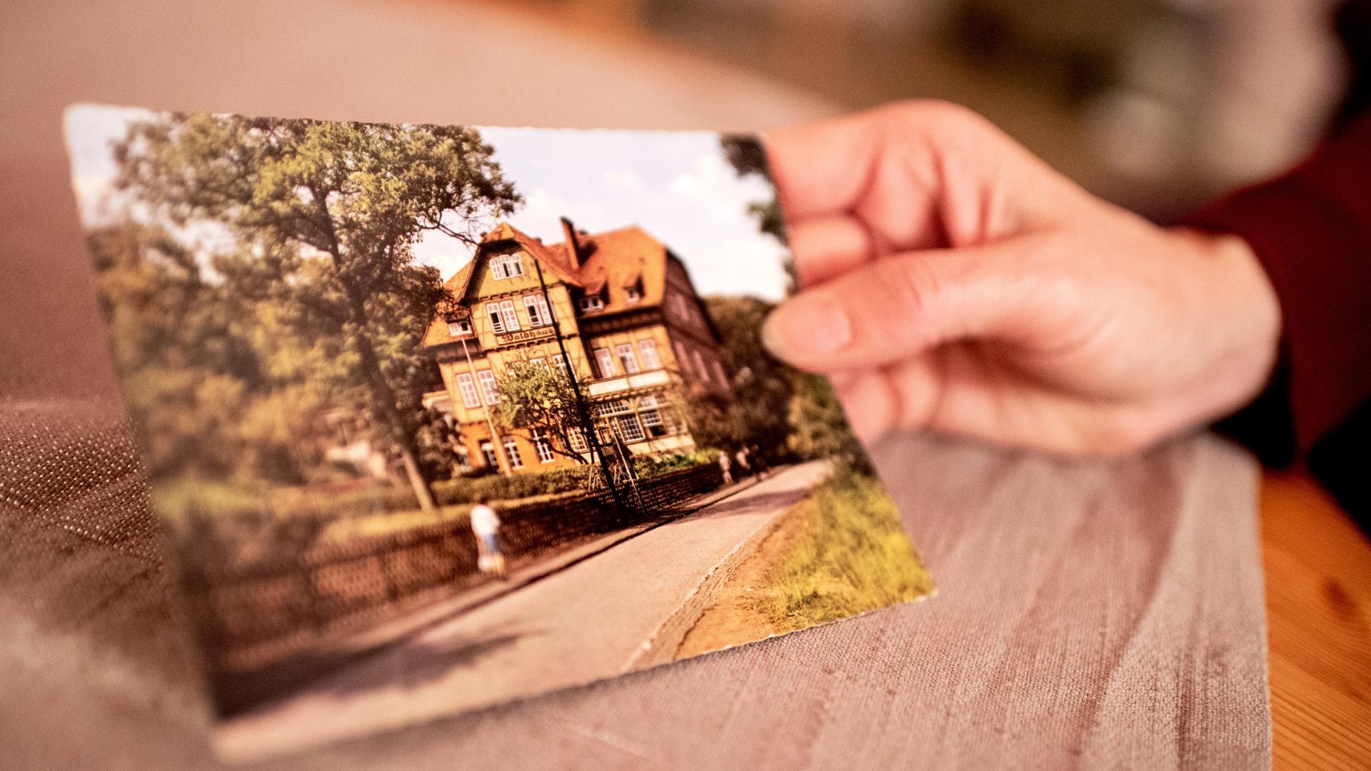 Eine Hand hält ein Foto eines mehrstöckigen Hauses.