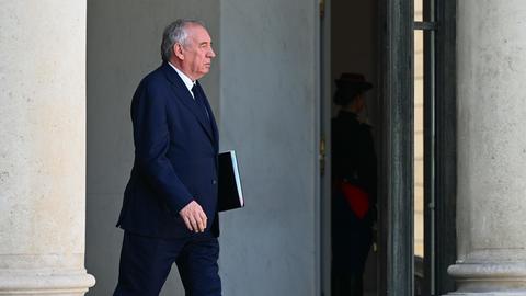 François Bayrou verlässt, eine Aktenmappe unter seinem Arm, ein Regierungsgebäude.